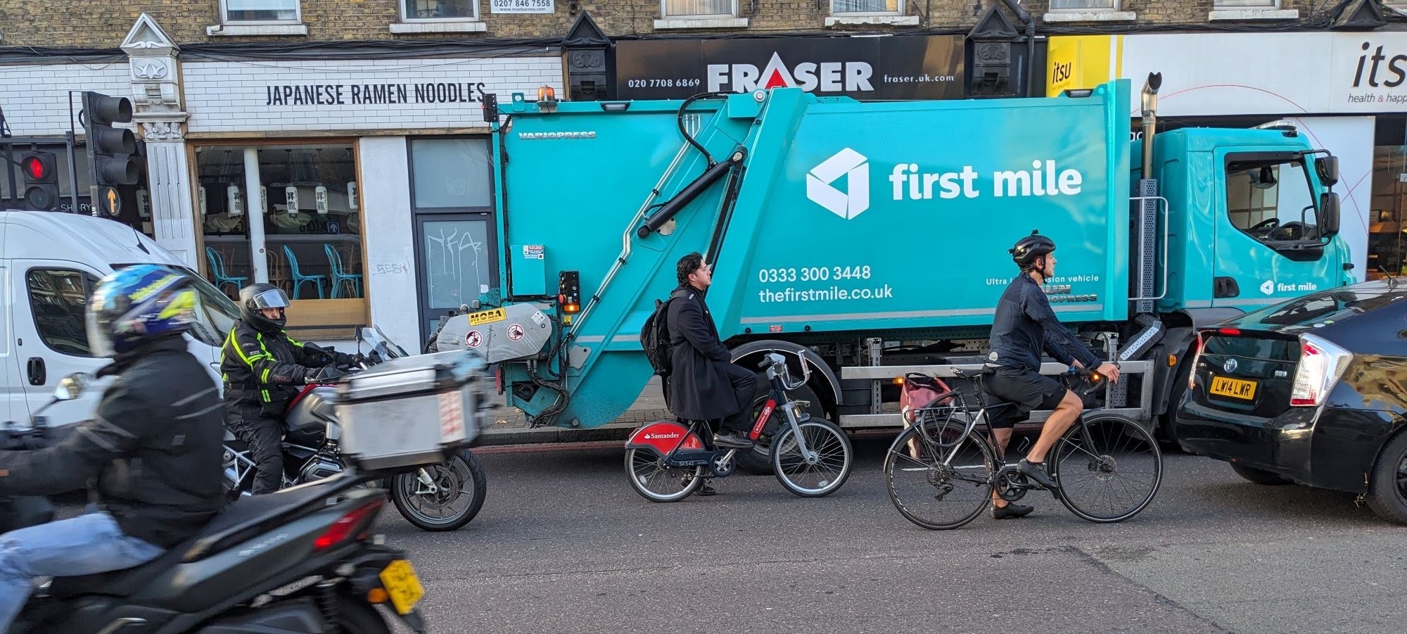 A street scene in Shoreditch with a bin lorry, people on bikes, and motorbikes.